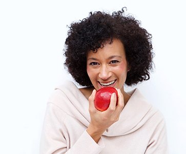 Smiling woman with dental implants biting into an apple on a white background
