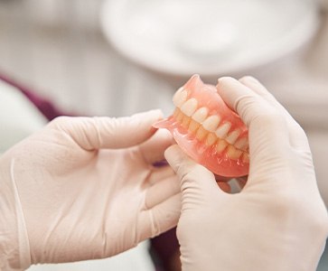 Gloved hands holding full set of dentures
