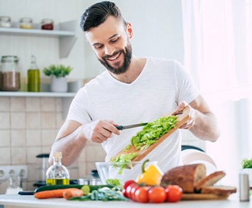 Man smiling while preparing salad in kitchen