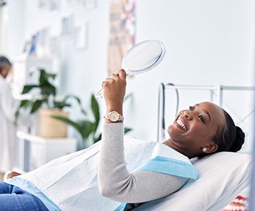 Woman smiling at reflection in handheld mirror