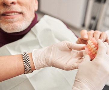 Gloved hands giving dentures to patient in dental chair