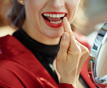 Closeup of a woman in a red jacket pointing to her new dental implant