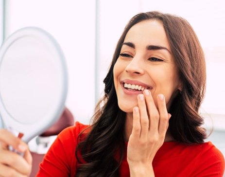 An older man admiring his new dental implant in a hand mirror