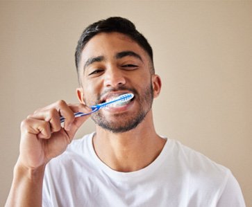 A handsome man brushing his teeth against a tan backdrop