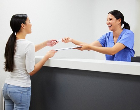 Dental assistant smiling while handing patient forms