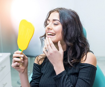 Woman smiling while looking at her teeth in handheld mirror