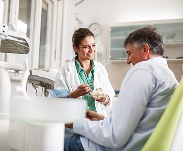 Woman smiling while looking at her teeth in handheld mirror
Female dentist smiling at patient during consultation
