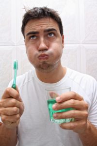 man holding toothbrush mouthwash while gargling 
