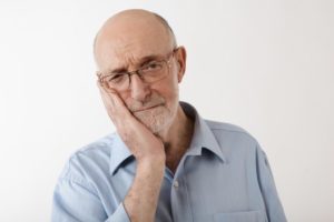 older man holding jaw in pain