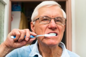 older man brushing teeth preventing dental implant infections