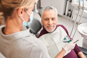 Man in maroon shirt smiling at dentist from the dental chair while she holds up a mold of his teeth