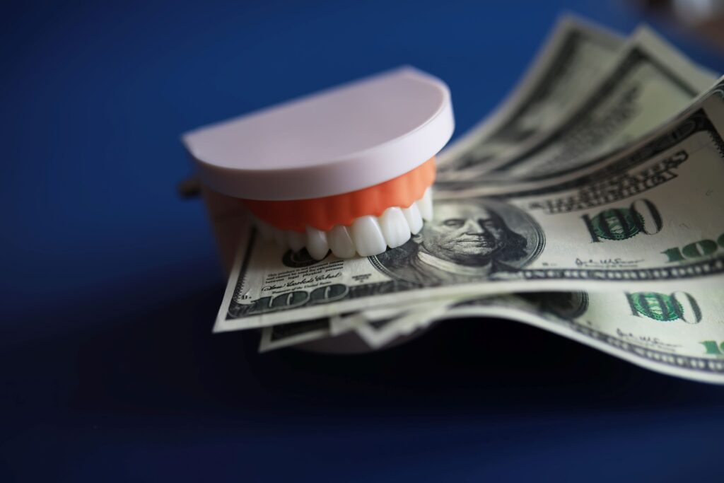 Artificial teeth holding $100 bills on dark blue surface