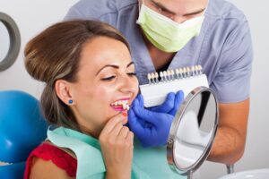Woman trying out veneers with dentist in background. 